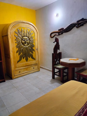 A room with a bed, a wooden cabinet with a sun design, a wooden chair, a small table, and a wall-mounted decoration. - Room-cancun Guest House 3 Near Ado bus t (Cancun)
