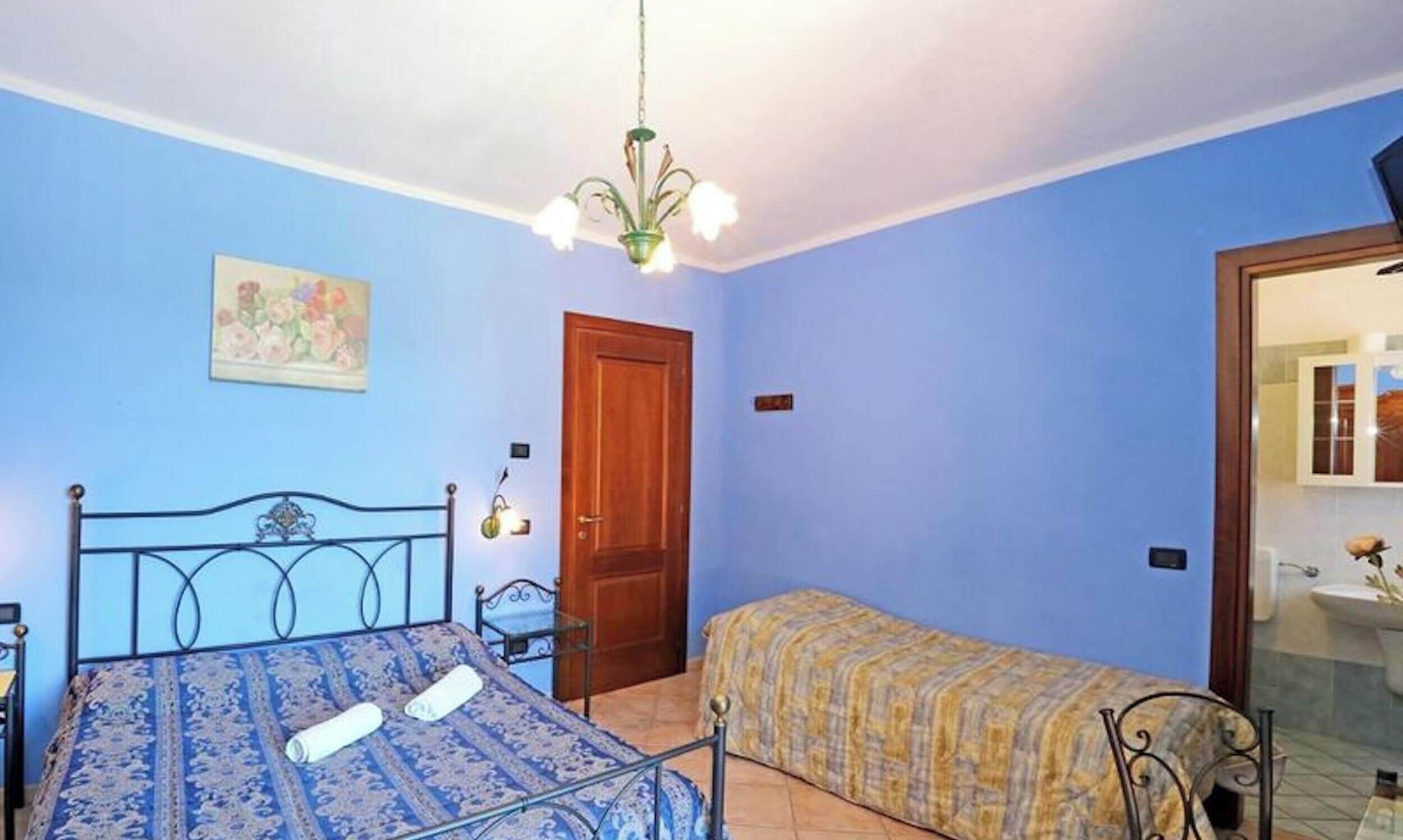 Une chambre à coucher avec un lit, une table de chevet, une chaise, une porte et une petite salle de bain visible à travers une porte ouverte.