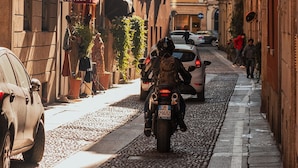 Una calle estrecha bordeada de edificios históricos, una tienda antigua y automóviles estacionados.