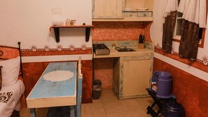 Una habitación pequeña y funcional con cama, mesa, kitchenette y ventana con cortinas.