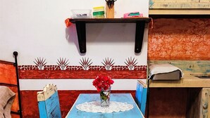 Una mesa azul con un copo de encaje, un florero con flores rojas y una repisa superior con utensilios de cocina.