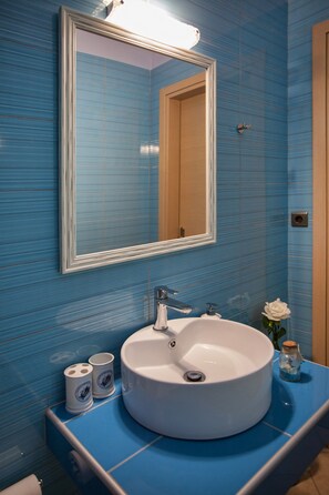 A bathroom with a round sink, a mirror, and blue tiled walls.