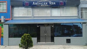 An American Visa Hotel with a blue awning, a small tree in front, and a closed entrance. - Hotel American Visa Bogota (Bogotá)