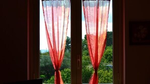 Quarto com duas janelas, cada uma com cortina de tule e um tecido vermelho fechado amarrado na parte inferior.