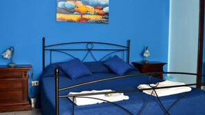 Quarto com parede azul, estrutura de cama em metal, cômoda de madeira e pintura de uma paisagem.