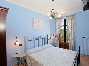 A bedroom with a bed, a small table, a nightstand, a window with curtains, a painting on the wall, and a radiator. - Room in B&B - Agriturismo Al Brich Single Room With Breakfast (Albaretto della Torre)