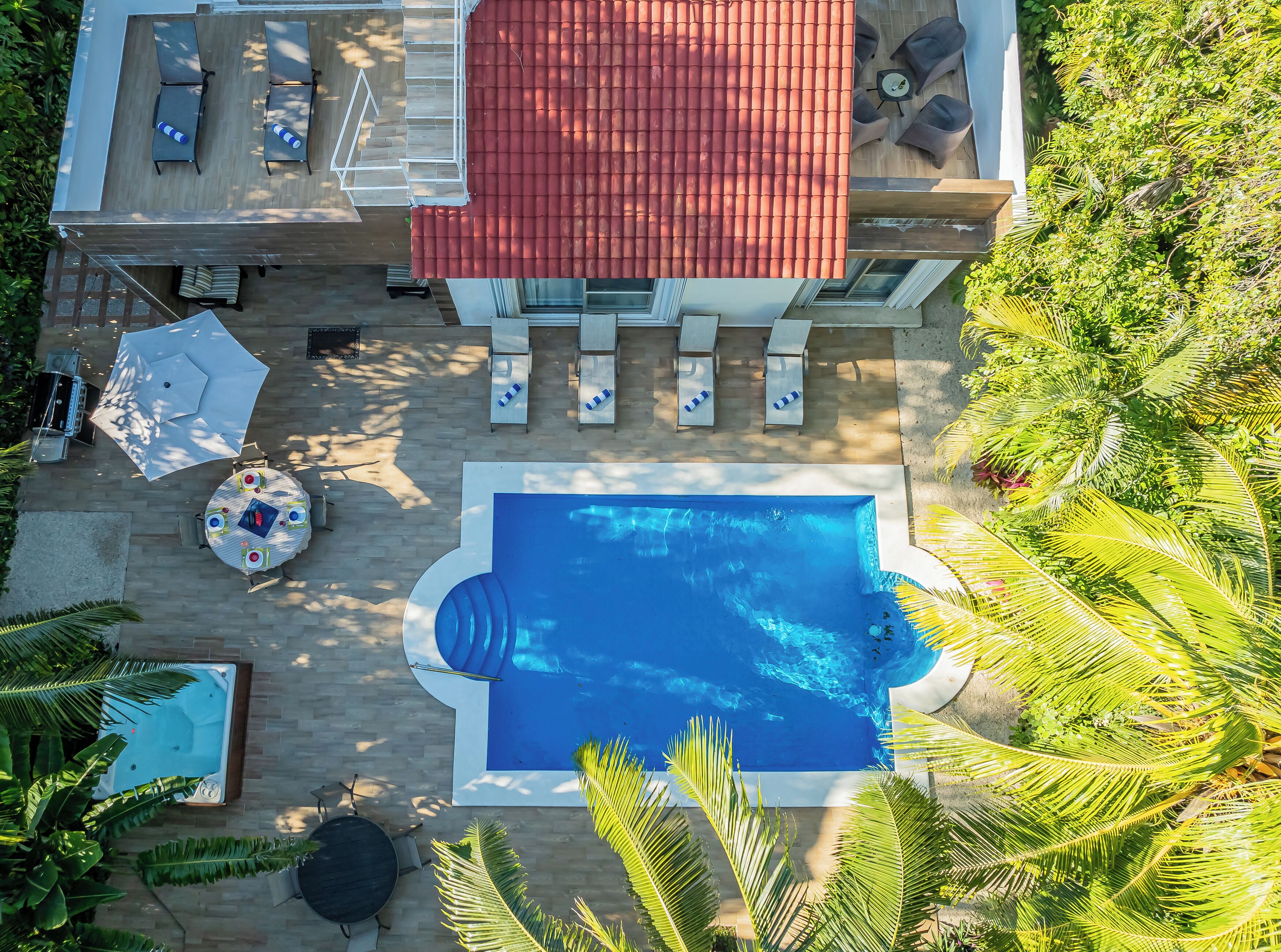 Un espace piscine aménagé sur le toit, avec des chaises longues, un jacuzzi et une table à manger.