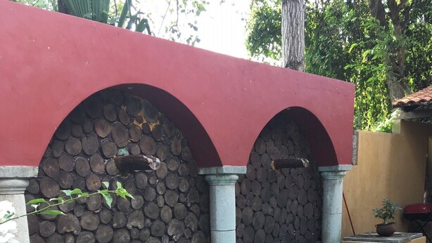 Piscina rectangular con borde de madera, rodeada por un muro de piedra con un arcojón rojo.