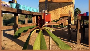 A rustic wooden structure with a woven roof, surrounded by a wooden fence and a large green plant in the foreground. - Room in Guest Room - Camp - Santos Cabanas (Todos Santos)
