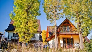 A traditional wooden house with a sloped roof, surrounded by tall trees and a fence.