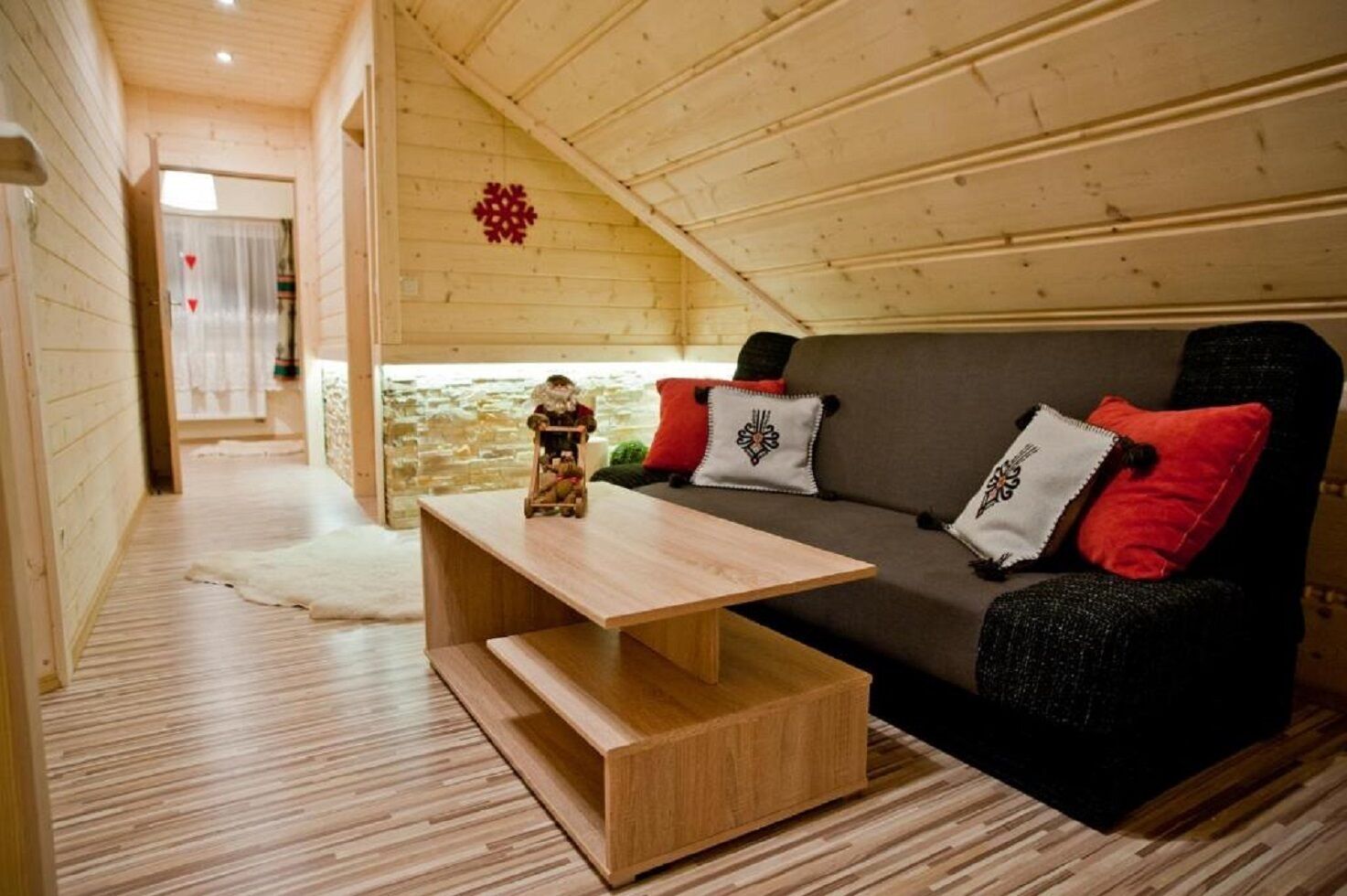 A cozy wooden cabin interior with a sofa, pillows, a small table, and a decorative item.