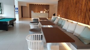 Un área de descanso moderna con mesa de billar, asientos con cojines y un mostrador de recepción.