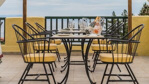 Un área de comedor al aire libre techada, con una mesa dispuesta para cuatro personas, rodeada de sillas con cojines amarillos, bajo una pérgola de madera con cortinas blancas.