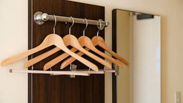 Un porte-manteaux en bois, muni de plusieurs cintres, est placé contre une porte en bois sombre, à côté d’un miroir.