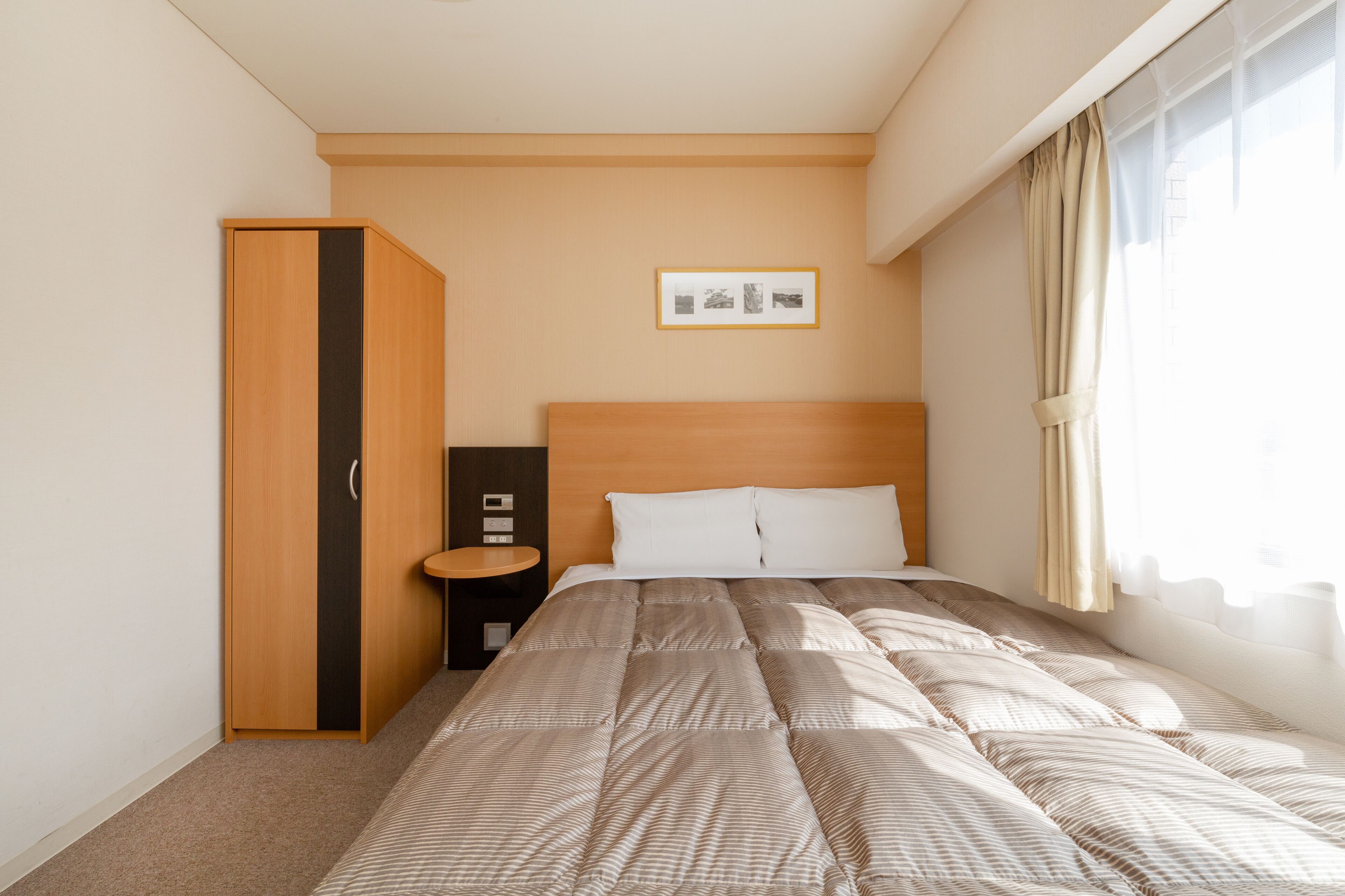 Een keurig opgemaakt slaapkamer met een bed, een kledingkast, een nachtkastje en een ingelijst foto aan de muur.