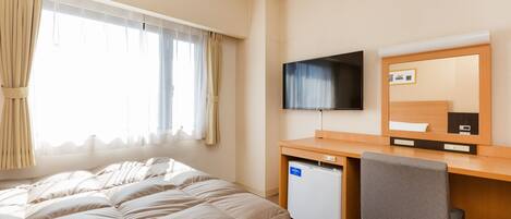 A hotel room with a bed, a desk with a computer, a TV, and a small refrigerator.