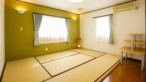 A room with tatami flooring, two windows with curtains, a small table, and a wall-mounted air conditioner.