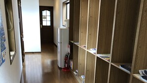 A hallway with wooden flooring, a white refrigerator, and wooden shelving units with magazines.