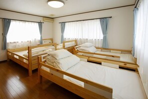 Une pièce avec trois lits superposés en bois, un luminaire au plafond et des fenêtres avec des rideaux.