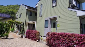 A row of green buildings with a covered entrance and a small garden area with pink flowers.