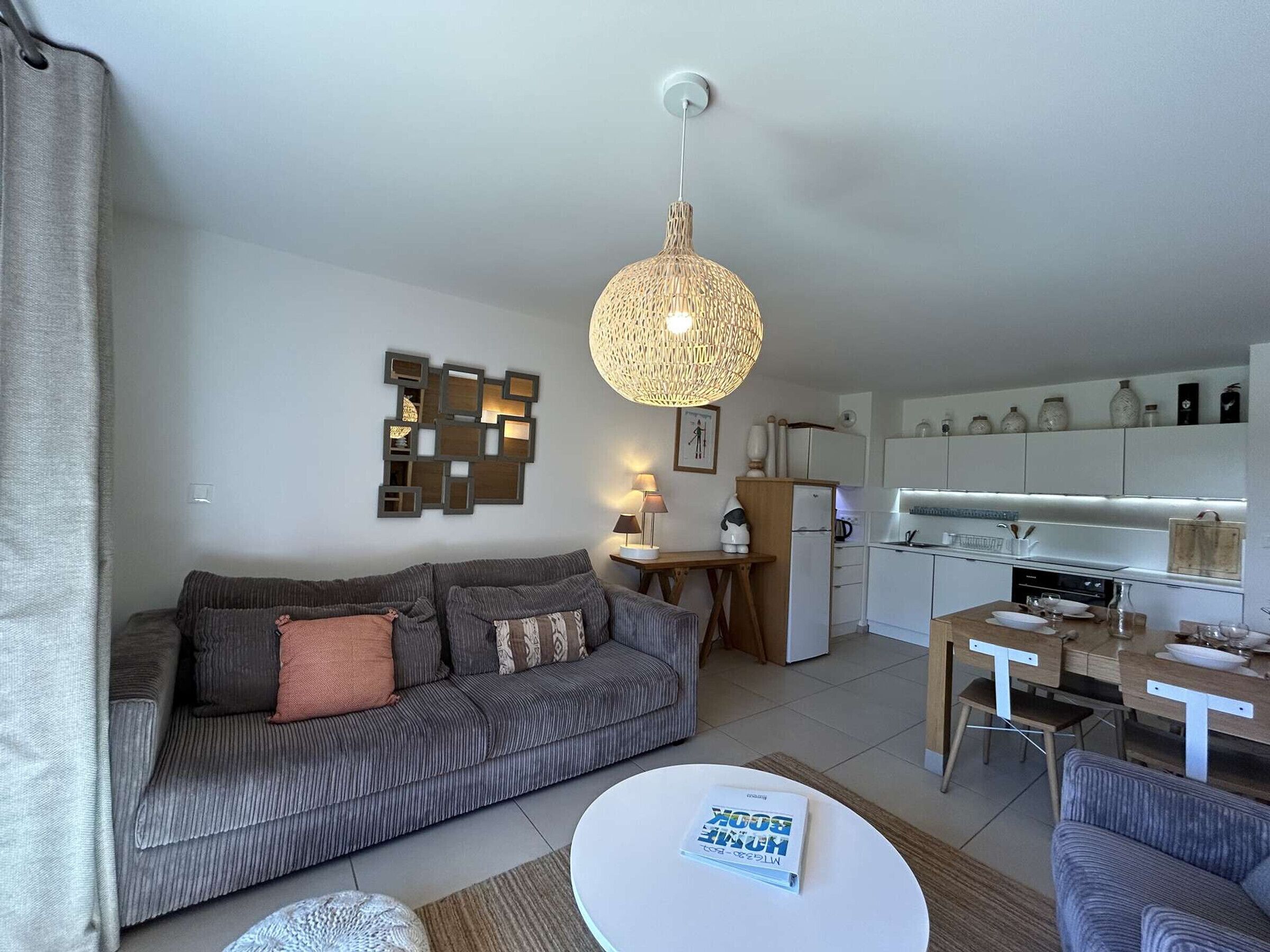 A modern living room with a sofa, a coffee table, and a dining area with a kitchen in the background.