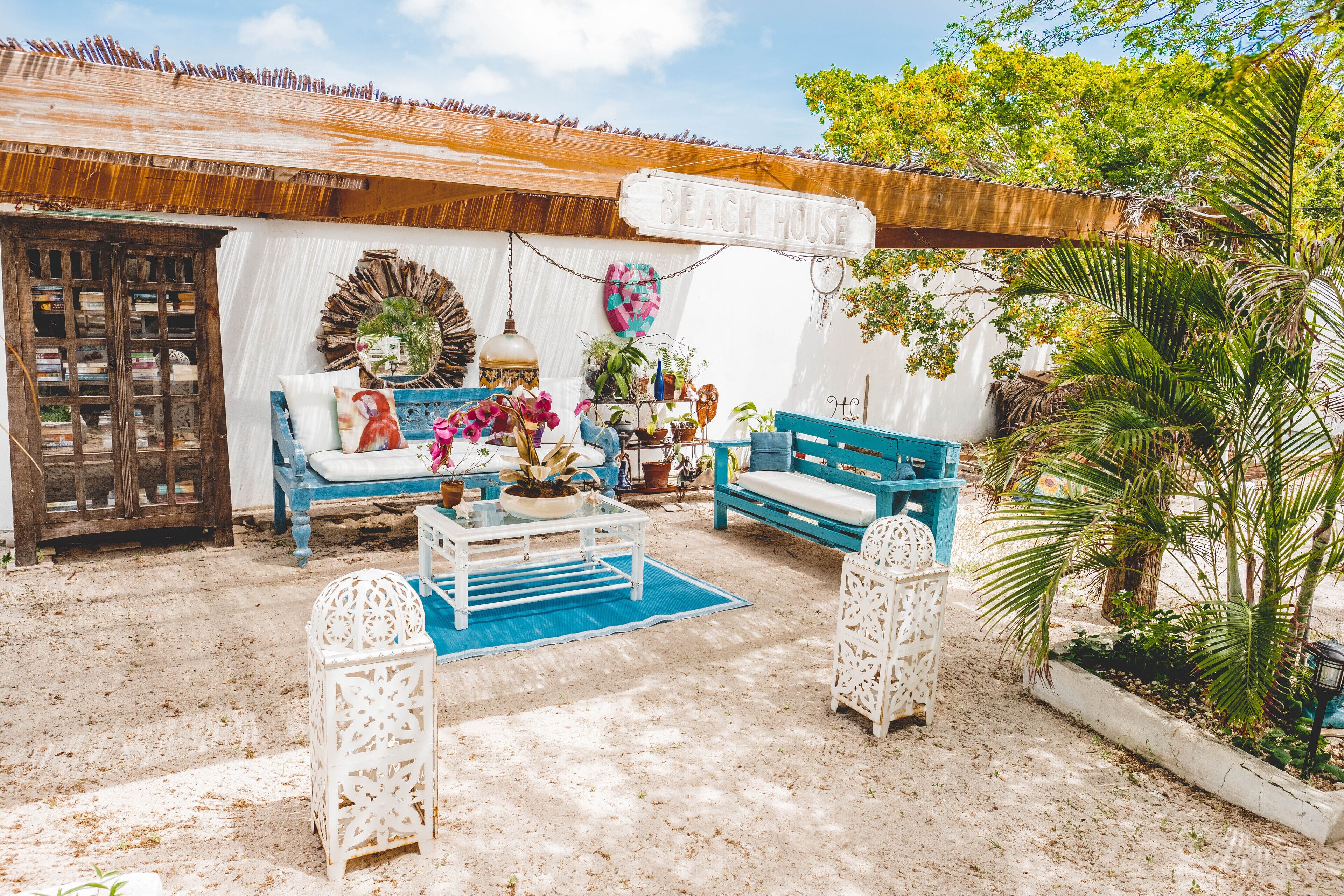 A beach house interior with a wooden ceiling, a white wall with a dreamcatcher, and a blue sofa.