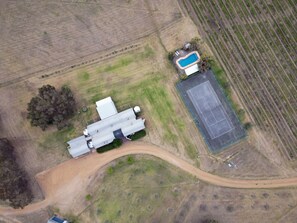 An aerial view of a property with a swimming pool, tennis court, and a large building with a garage.
