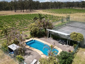 A pool area with a covered patio and outdoor seating, surrounded by a fenced garden and a vineyard in the background.