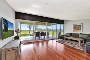 A spacious living room with a large sliding glass door leading to an outdoor area, a wooden coffee table, a sofa, and a painting on the wall. - Ironbark Hill TJD Retreat (Pokolbin)