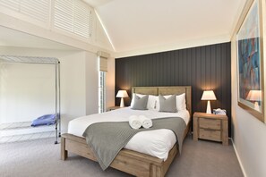 A hotel room with a large bed, two bedside tables, a wooden headboard, a wall-mounted artwork, and a balcony with a metal railing.