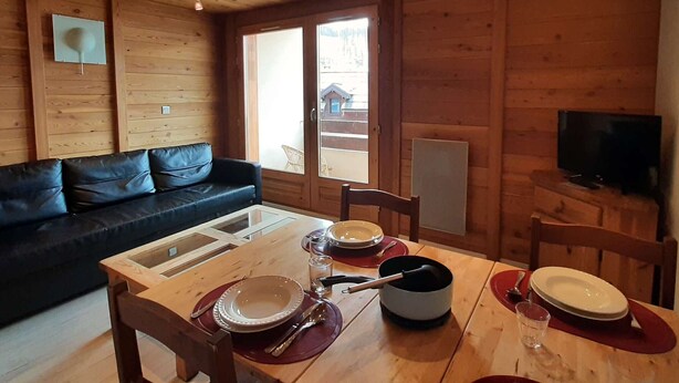 L'intérieur d'un chalet en bois comprend une table à manger pour quatre personnes, un canapé et un téléviseur fixé au mur.