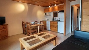 Une cuisine compacte avec des meubles en bois, un four à micro-ondes et une machine à café. On y trouve une table à manger avec des chaises et un banc.