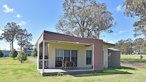 A single-story house with a covered porch, a dining area with a table and chairs, and a small shed attached to the right. - Ironbark Hill Spa Bath Villa 1- Tyrian (Pokolbin)