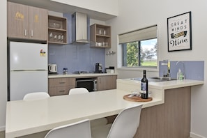 A modern kitchen with a central island, built-in appliances, and a window with a view. - Ironbark Hill Villa 3 - Saperavi (Pokolbin)
