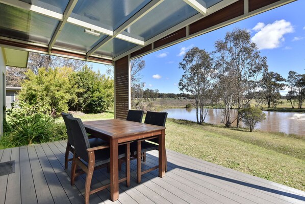 An outdoor deck with a wooden table and chairs, overlooking a body of water and trees.