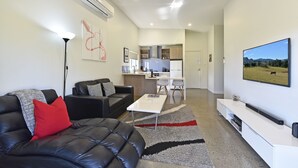 A modern living room with a black leather sofa, a coffee table, and a flat-screen TV mounted on the wall. - Ironbark Hill Spa Bath Villa 4 - Novato (Pokolbin)