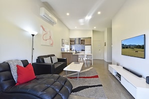 A modern living room with a black leather sofa, a coffee table, and a flat-screen TV mounted on the wall. - Ironbark Hill Spa Bath Villa 4 - Novato (Pokolbin)