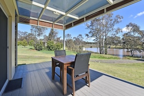 An outdoor deck with a table and chairs, overlooking a grassy area and a body of water.