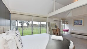 A bedroom with a large bed, a desk, and a view of a green field. - Ironbark Hill Estate (Pokolbin)