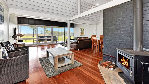 A spacious living room with a fireplace, a large window, and a view of the outdoors. - Ironbark Hill Estate (Pokolbin)