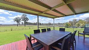 A covered outdoor seating area with a table and chairs, overlooking a grassy field and trees. - Ironbark Hill Estate (Pokolbin)
