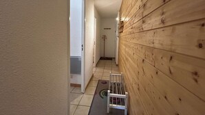 Un couloir étroit, avec un lambris en bois sur un côté et une porte blanche au fond.