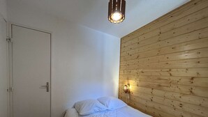 Un lit simple avec une couette blanche, dans une pièce dont un mur est recouvert de panneaux de bois et qui possède une porte.