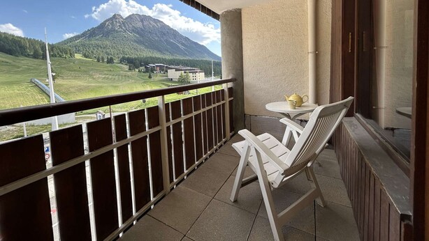 Un balcon donnant sur une montagne, une chaise, une table et une théière.