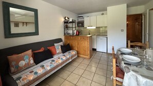 Un espace de vie compact comprenant un canapé, une table à manger pour quatre personnes, une kitchenette et un miroir mural.