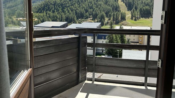A balcony with a view of a forested mountain range and buildings in the background. - Cozy 2-Room Apartment with Mountain View, Balcony, and Parking in Montgenèvre - Sleeps 6 (Montgenèvre)
