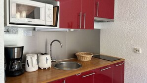 A compact kitchen with red cabinets, a white microwave, a sink, a coffee maker, and a toaster. - Cozy 2-Room Apartment with Mountain View, Balcony, and Parking in Montgenèvre - Sleeps 6 (Montgenèvre)