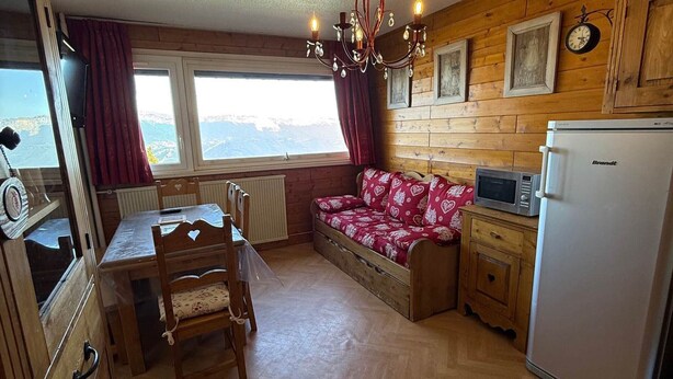 A cozy kitchen with wooden walls, a dining table with chairs, a sofa, a refrigerator, and a window with curtains. - 2-room rental for 5 people at the foot of the slopes (Les Adrets-Prapoutel)