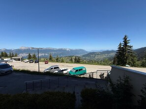 Uma área de estacionamento com veículos, um edifício e uma paisagem montanhosa ao fundo.