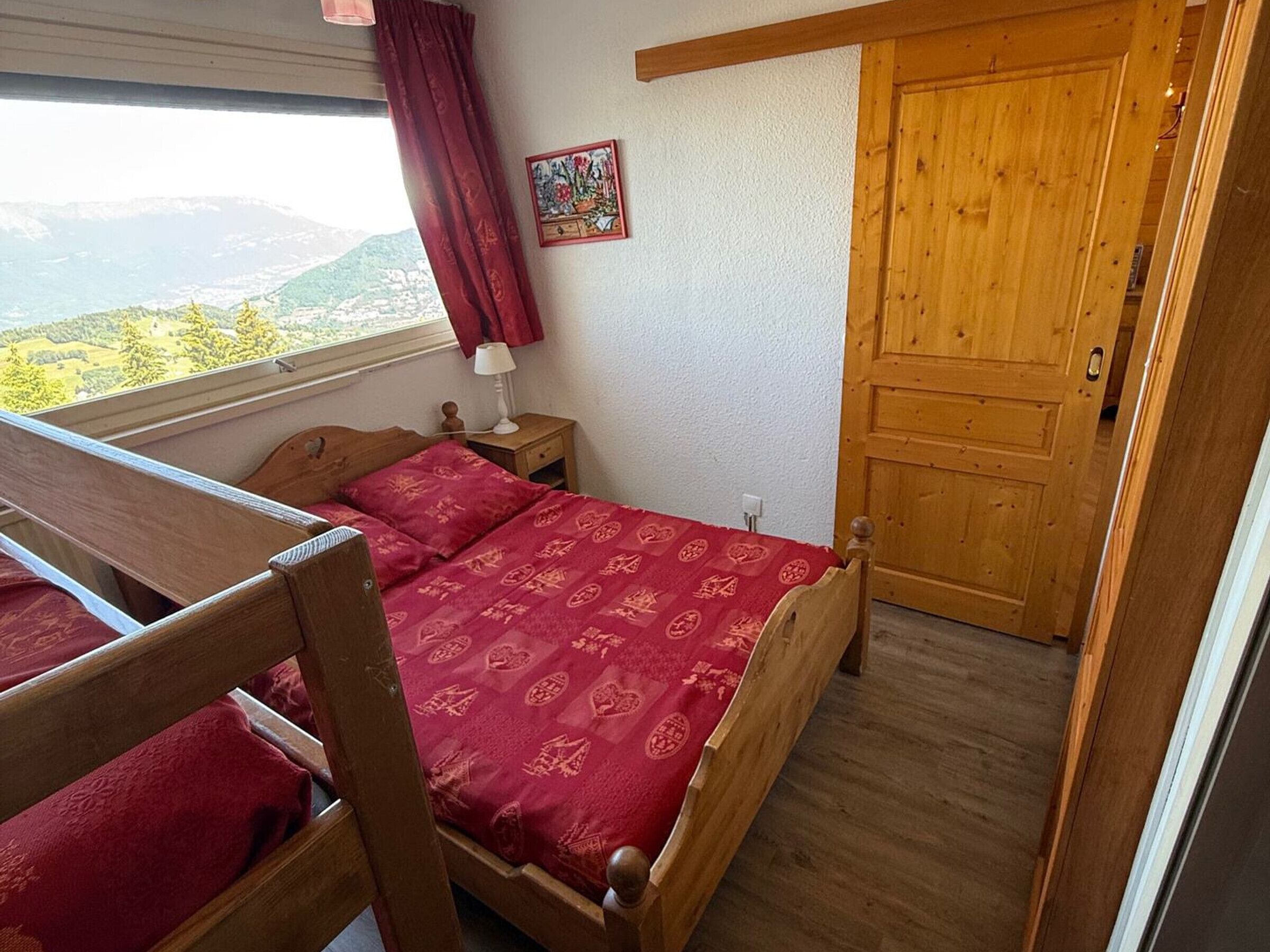 Une chambre à coucher avec un lit en bois, une table de chevet, une lampe, une fenêtre donnant sur un beau paysage et une porte.